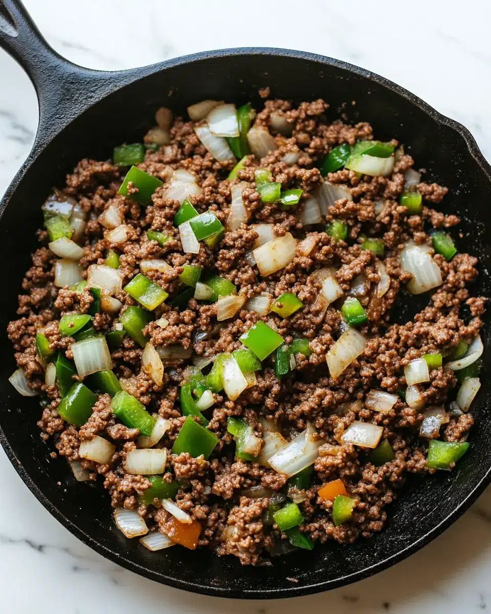 sauteed-beef-green-peppers-onions-skillet Ground beef, green bell peppers, and onions sautéing in a cast iron skillet